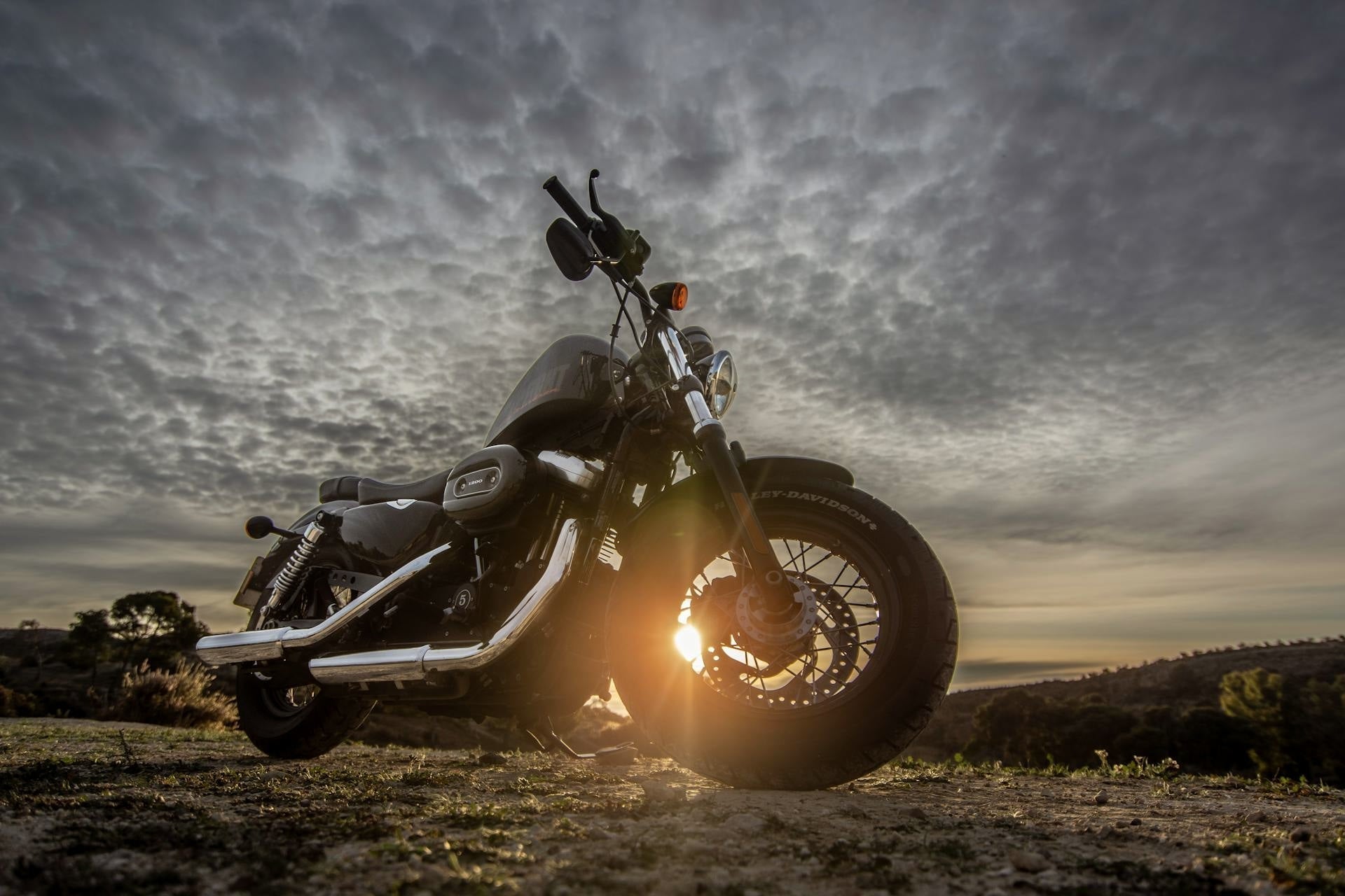 Black Harley-Davidson motorcycle at sunset on open terrain with dramatic clouds in the sky