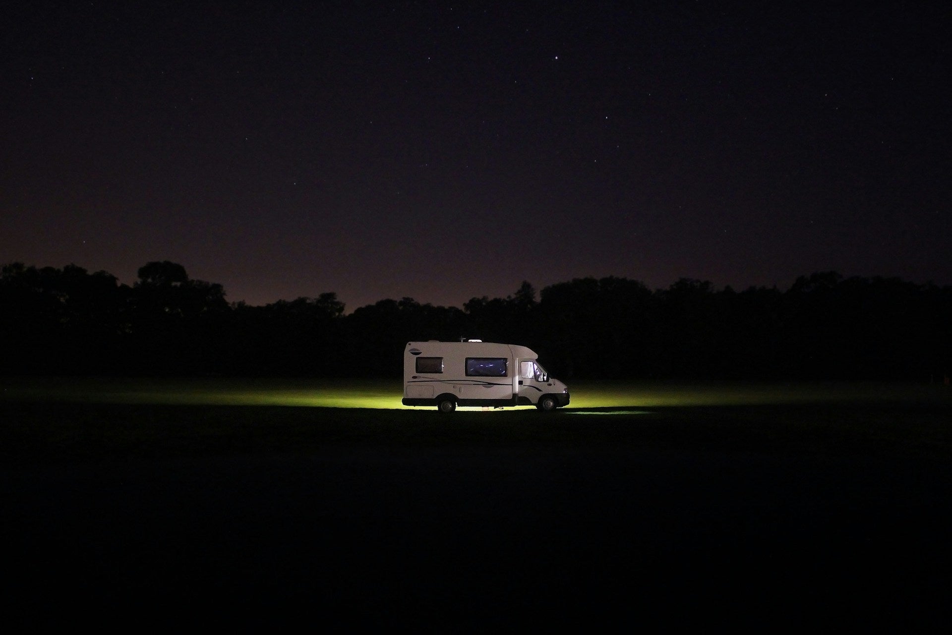 A lone RV illuminated in a dark field at night, symbolizing remote travel, boondocking, and the need for GPS tracking to ensure peace of mind while parked in isolated locations