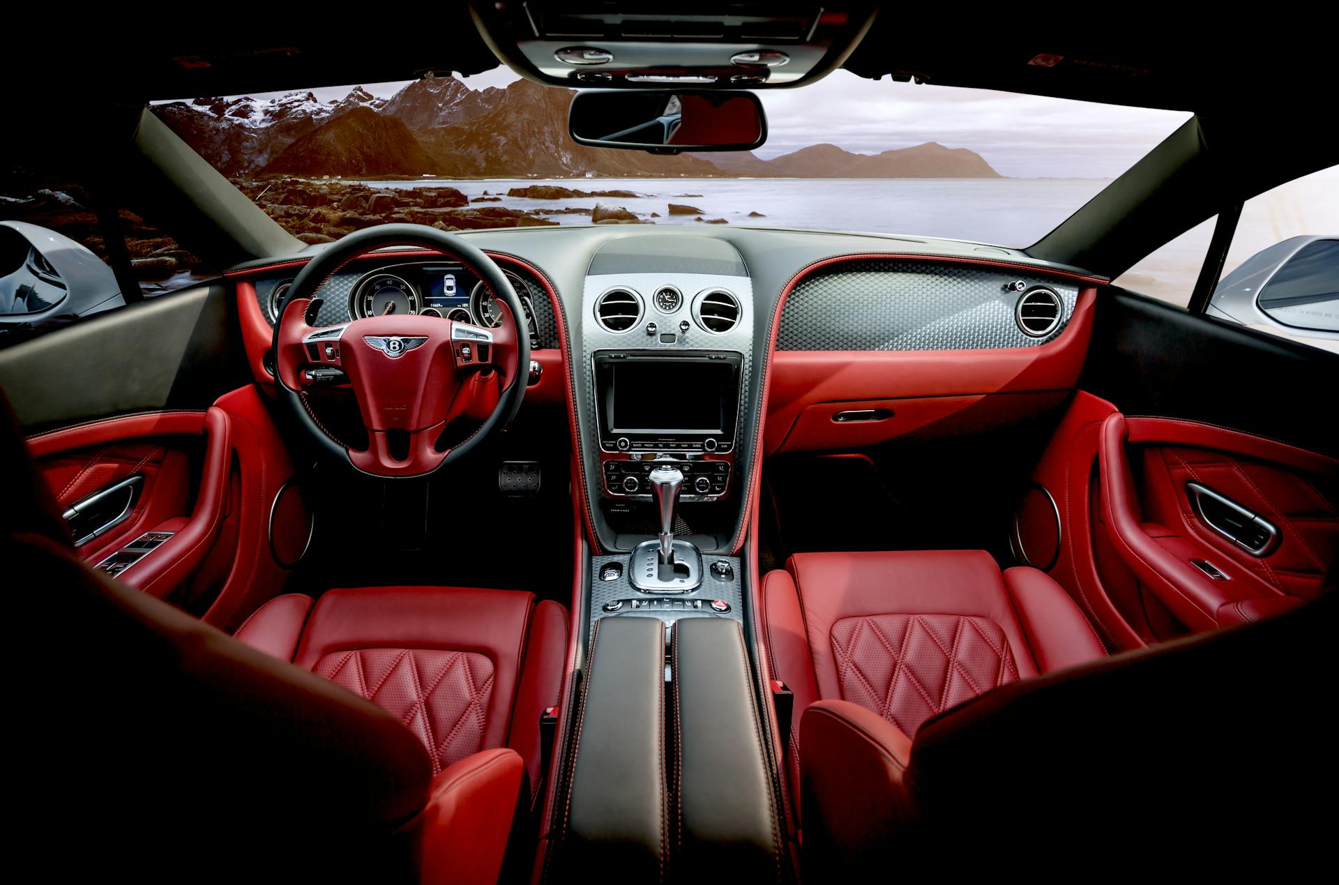 Interior view of a luxury car with red leather seats, steering wheel, and dashboard.